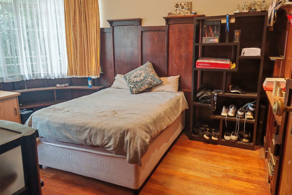 A bedroom featuring original timber wall paneling, hardwood flooring, and a built-in shelving unit, offering a classic aesthetic with potential for modernization.