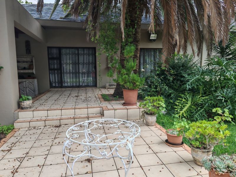 A covered patio area featuring tiled flooring, sliding glass doors with security gates, and built-in shelving, overlooking a garden space.