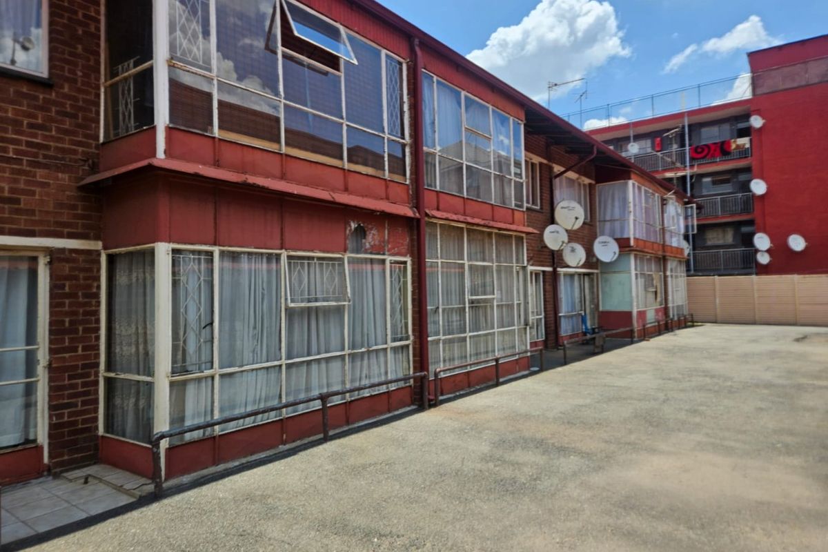 Rear exterior view of a multi-story apartment building featuring brick masonry, extensive metal-framed glazing, and paved common area.