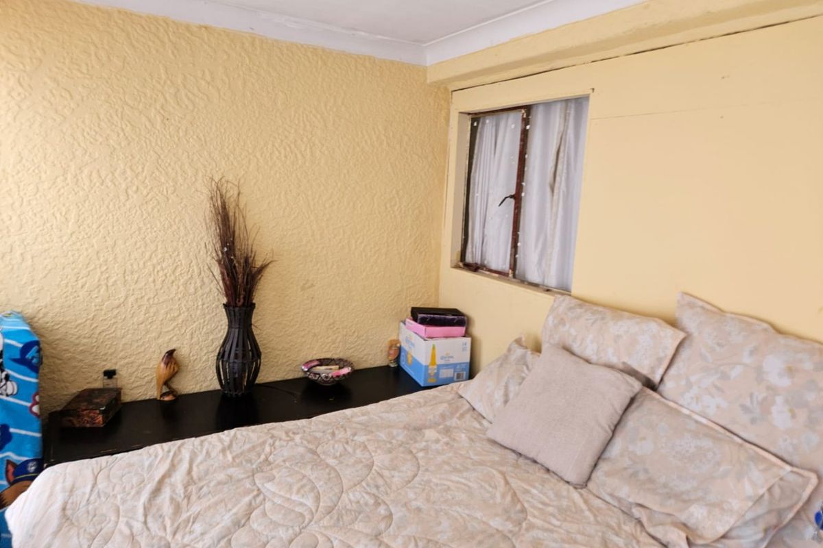 A bedroom featuring textured yellow walls, cove cornicing, and a standard casement window. The space requires cosmetic updates to modernize the finishes.