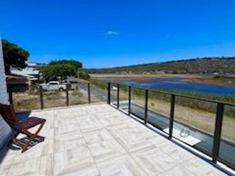 A spacious outdoor balcony featuring modern tiled flooring and a sleek glass balustrade, offering expansive views of the surrounding landscape and water.