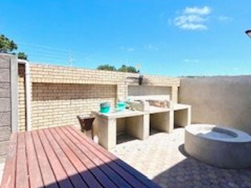 Outdoor patio area featuring a built-in braai, concrete fire pit, and paved flooring, enclosed by a brick boundary wall.