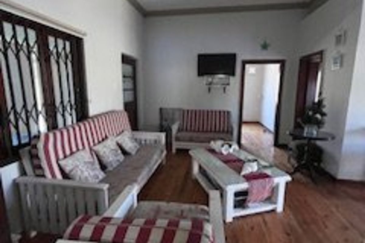 A living room featuring hardwood flooring, decorative ceiling cornices, and a security gate over the window.