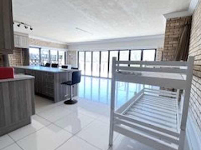 Spacious open-plan living and kitchen area featuring modern cabinetry, a large island, tiled floors, and expansive bi-fold doors leading to the outdoors.