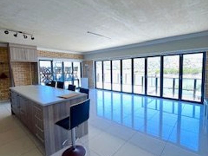 Spacious open-plan living area featuring a modern kitchen island, large bi-fold doors opening to the exterior, and polished tiled flooring.