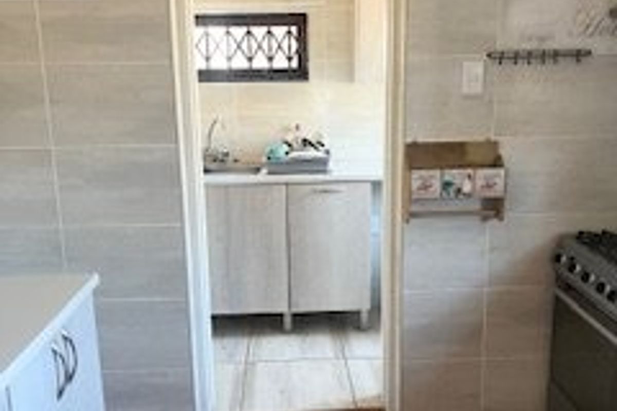 A kitchen area featuring timber flooring, tiled walls, and built-in cabinetry, with an adjacent scullery or prep area visible through the doorway.