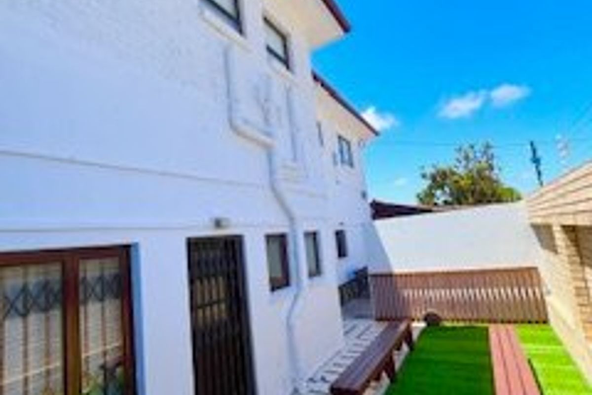 A rear exterior view of the property featuring a low-maintenance artificial lawn area, secure access points, and perimeter boundary walls.