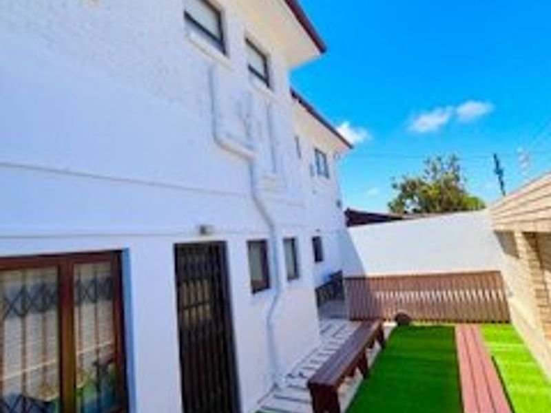 A rear exterior view of the property featuring a low-maintenance artificial lawn area, secure access points, and perimeter boundary walls.