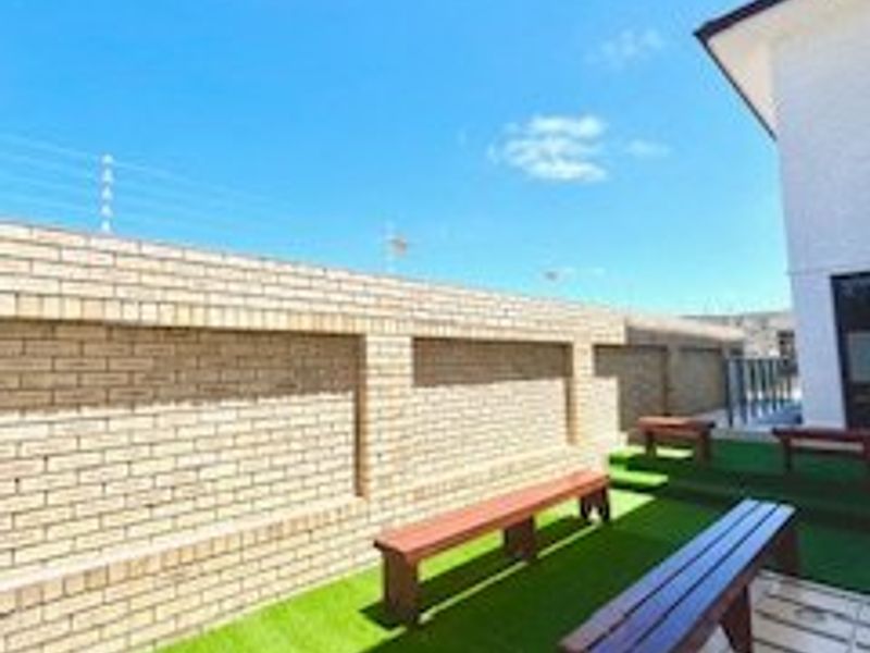 A clean outdoor patio area featuring a brick boundary wall, tiled flooring, and artificial turf, providing a low-maintenance space for outdoor relaxation.