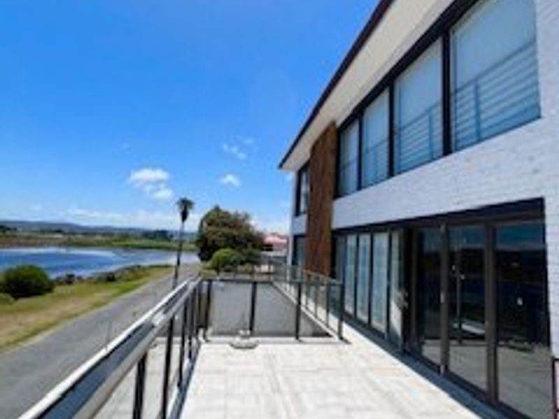 Spacious modern balcony featuring glass balustrades, tiled flooring, and large sliding doors with scenic water views.