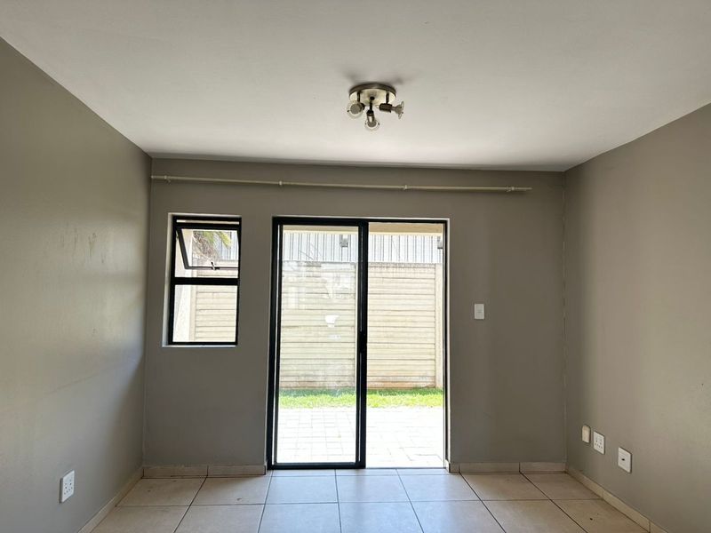 A bright, empty living area featuring neutral wall tones, tiled flooring, and a sliding glass door providing direct access to the outdoor patio area.