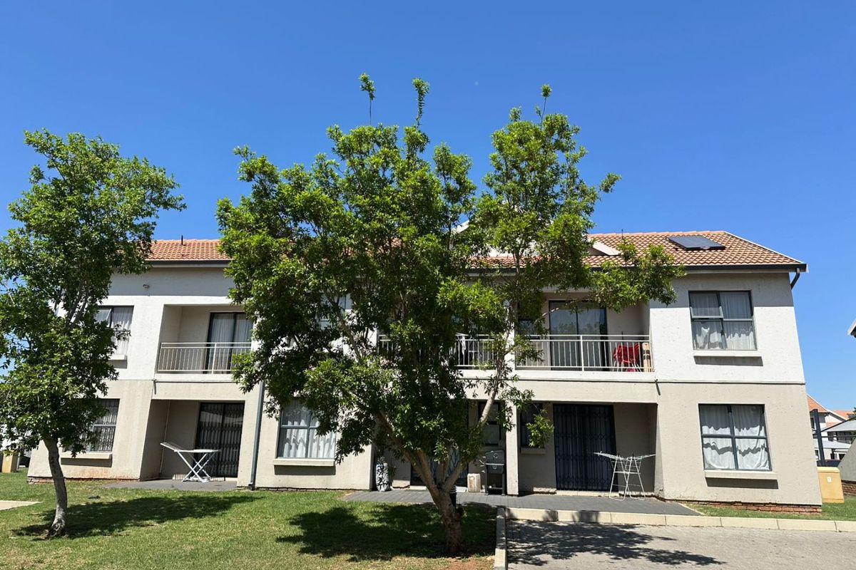 A view of the rear exterior elevation of a two-story apartment building featuring balconies, tiled roofing, and solar panels, set against a landscaped garden area.