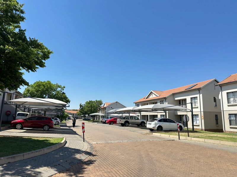 A view of the apartment complex exterior featuring paved driveways, covered parking bays, and well-maintained residential buildings under a clear blue sky.