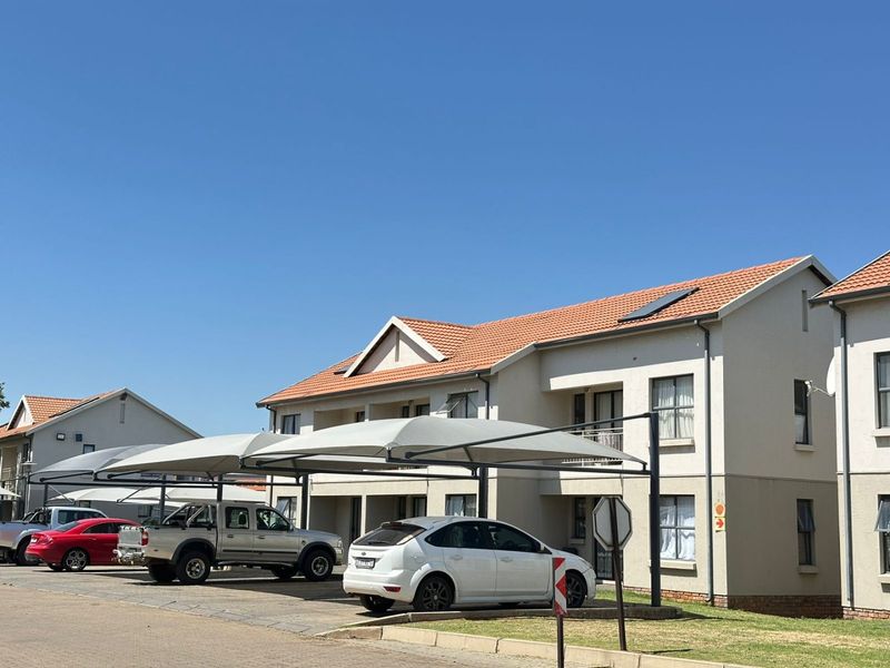 Exterior view of a multi-story apartment complex featuring tiled roofing, shaded parking bays, and paved driveway areas.