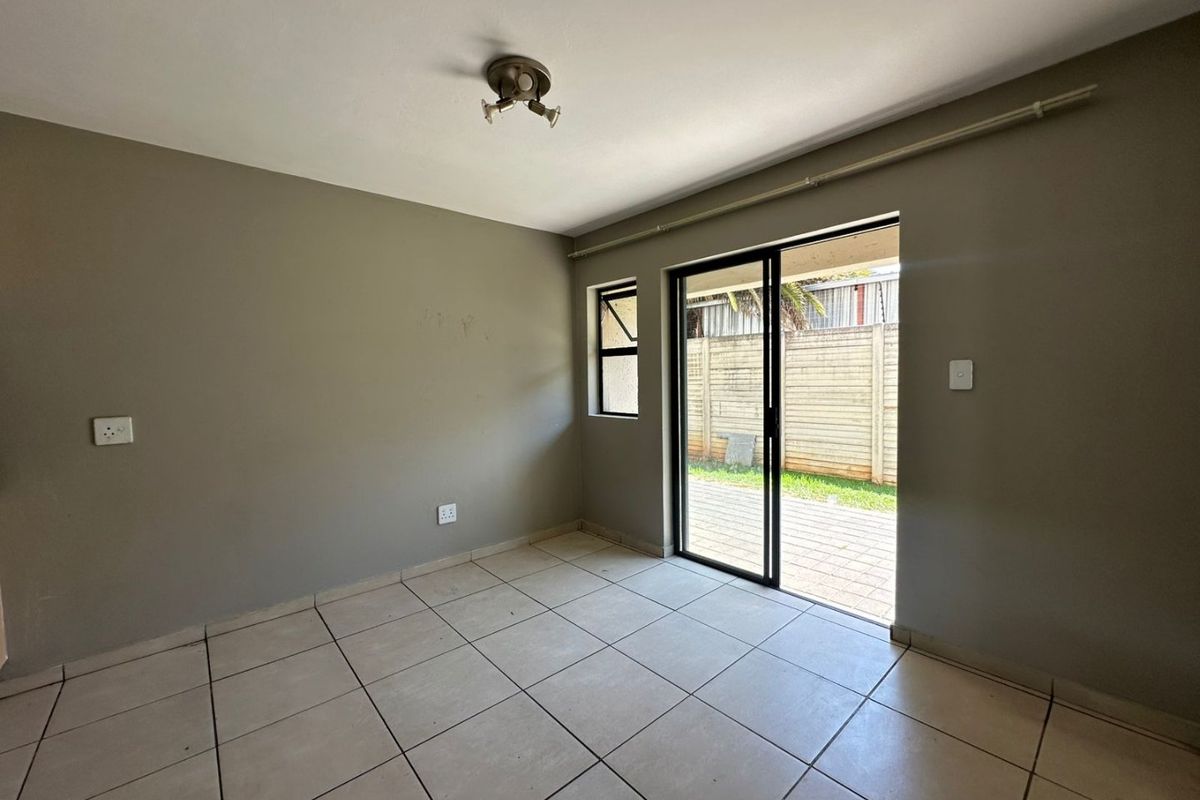 An empty living room featuring neutral tiled flooring, a ceiling-mounted light fixture, and sliding glass doors providing direct access to an outdoor patio area.