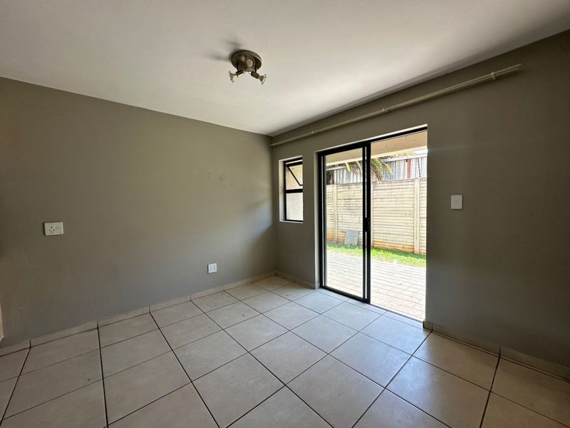 An empty living room featuring neutral tiled flooring, a ceiling-mounted light fixture, and sliding glass doors providing direct access to an outdoor patio area.