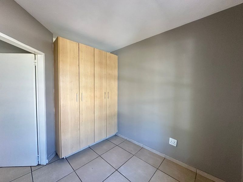 A bedroom featuring light wood-finish built-in cupboards, neutral grey walls, and tiled flooring.