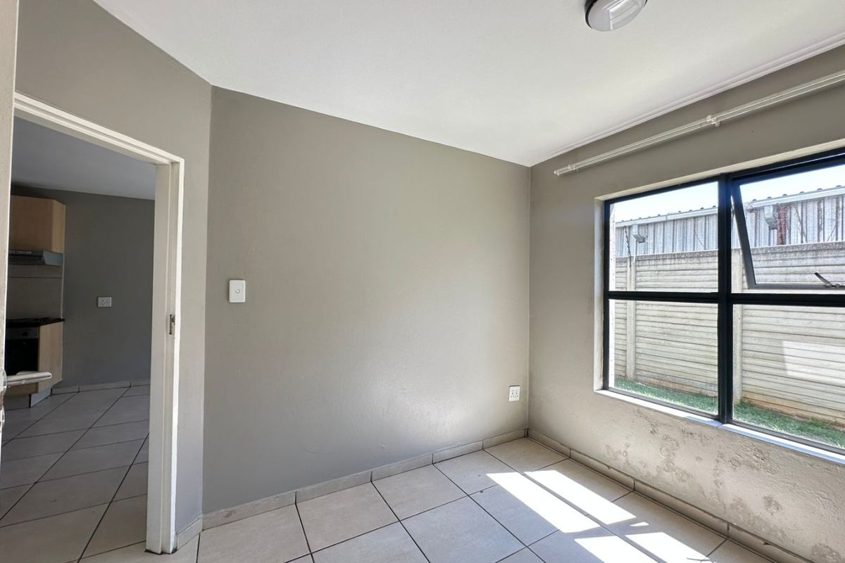 A vacant bedroom featuring tiled flooring, neutral wall paint, and a window with a view of the exterior boundary wall.