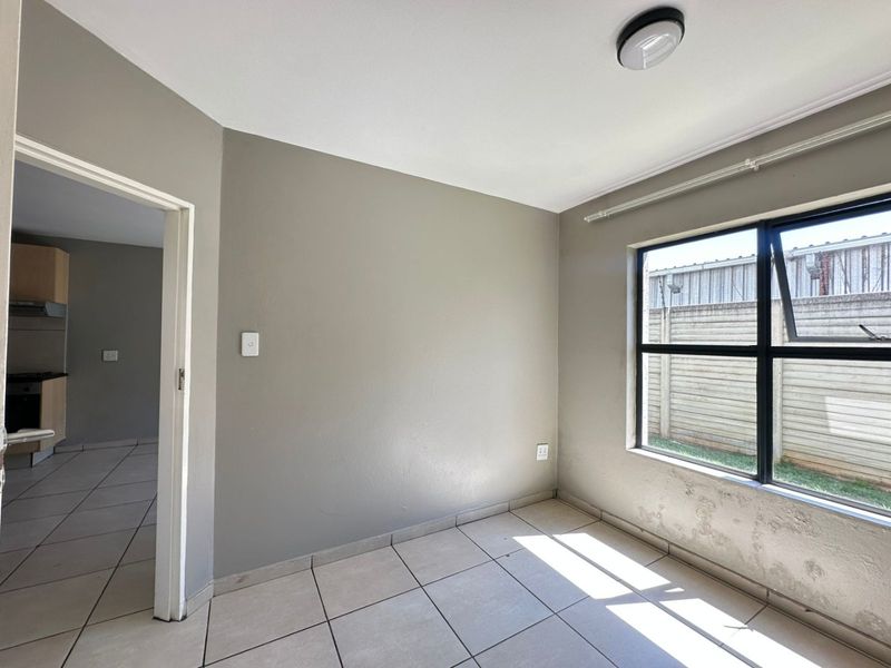 A vacant bedroom featuring tiled flooring, neutral wall paint, and a window with a view of the exterior boundary wall.