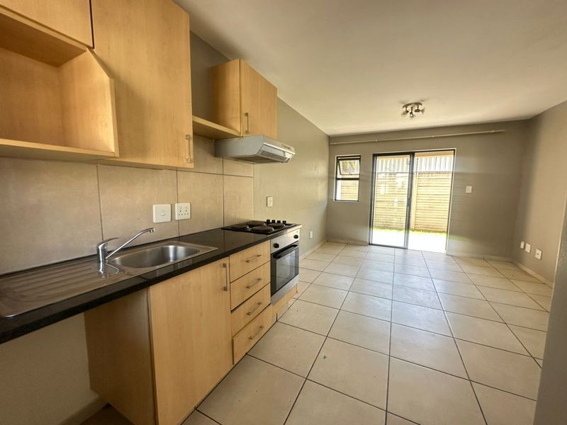 Open plan kitchen and living area featuring light wood cabinetry, built-in oven and hob, tiled flooring, and sliding door access to the rear exterior.