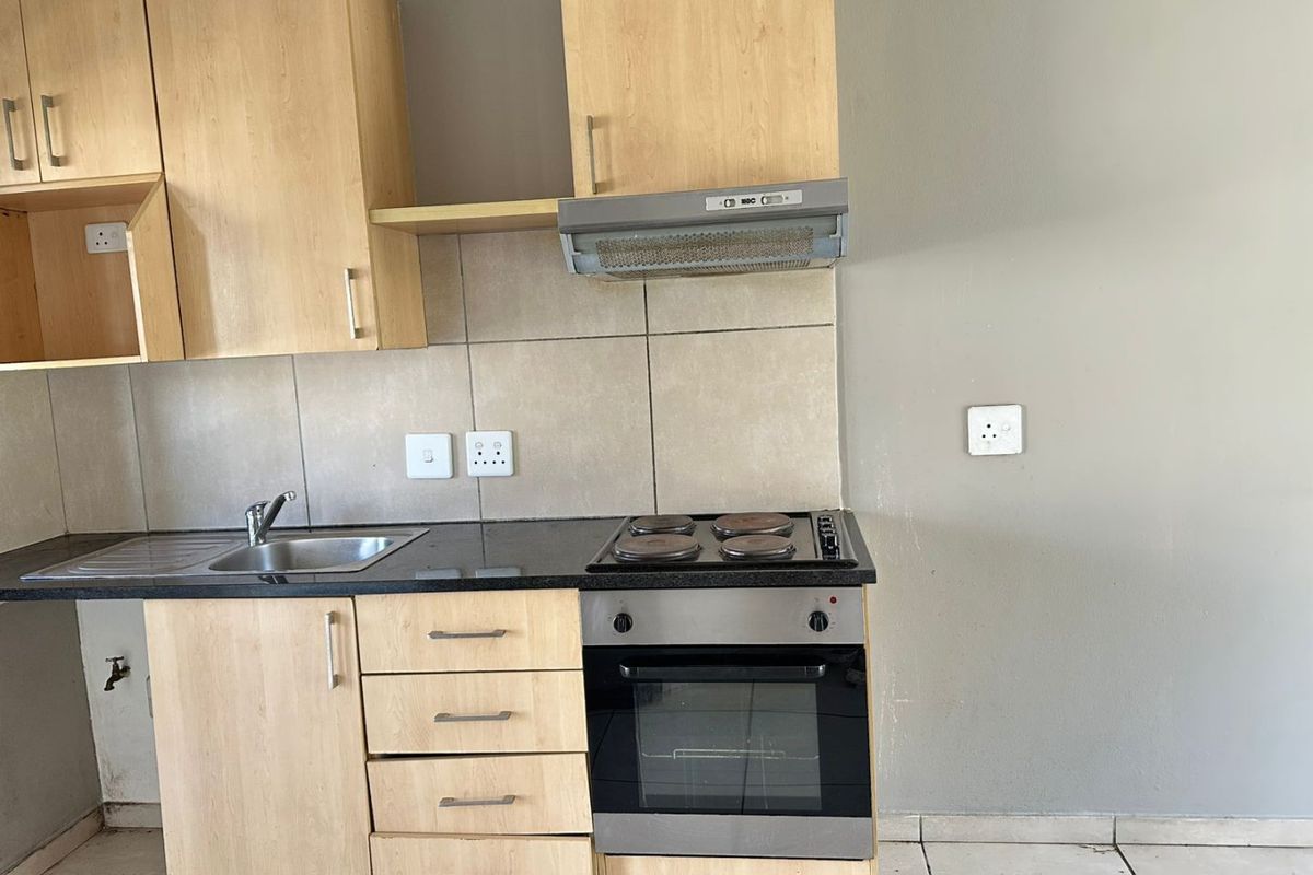 A functional kitchen featuring light wood cabinetry, a black granite countertop, a built-in oven with a four-plate hob, and a stainless steel sink.