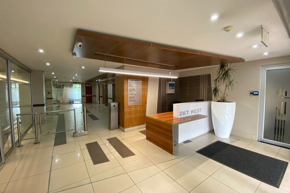 Modern commercial building lobby featuring a reception desk, tiled flooring, recessed lighting, and secure access turnstiles.