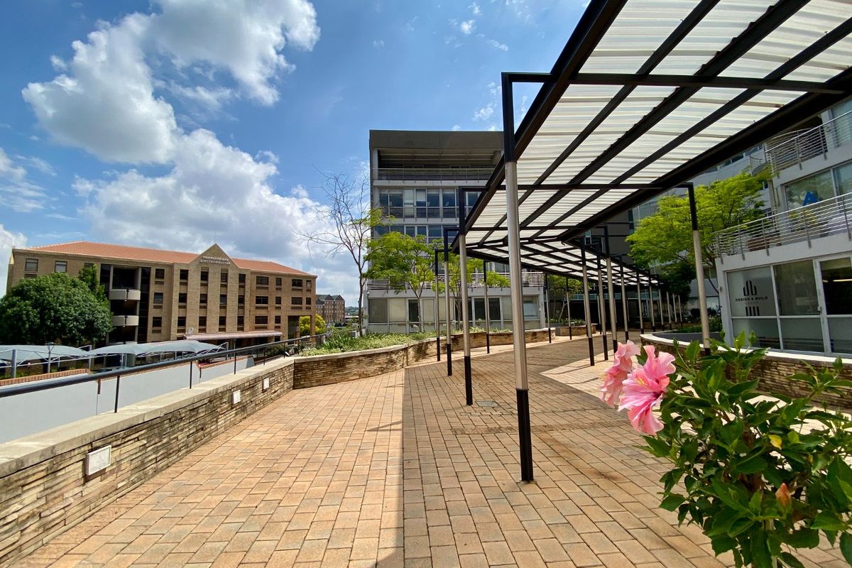 A spacious outdoor terrace featuring a modern metal pergola with translucent roofing, stone-clad retaining walls, and paved flooring in a commercial setting.
