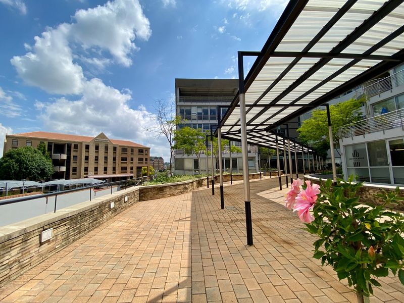 A spacious outdoor terrace featuring a modern metal pergola with translucent roofing, stone-clad retaining walls, and paved flooring in a commercial setting.