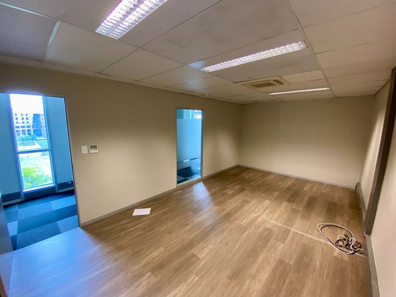 An empty commercial office space featuring laminate flooring, suspended ceilings with recessed lighting, and integrated air conditioning.