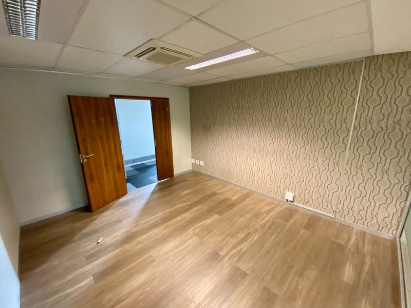 A vacant commercial office space featuring laminate flooring, a patterned feature wall, suspended ceiling with integrated lighting, and a ducted air conditioning unit.