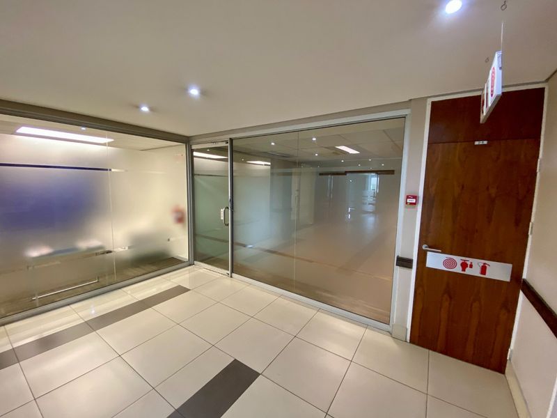 Modern commercial office space featuring glass partitioning, recessed lighting, and clean ceramic tiled flooring, providing a professional and bright work environment.