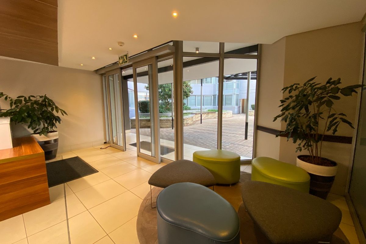 Modern commercial building entrance lobby featuring tiled flooring, recessed lighting, and large sliding glass doors providing access to an outdoor courtyard area.