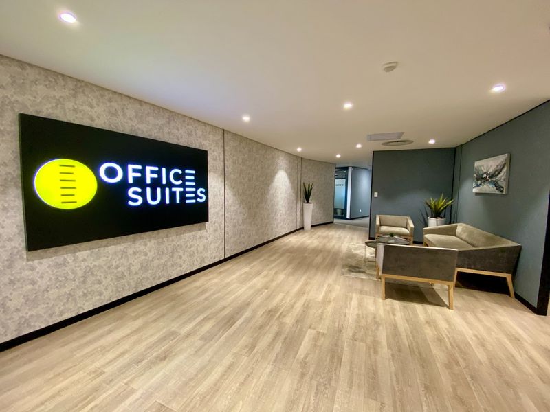 Modern commercial office building entrance lobby featuring wood-look laminate flooring, recessed lighting, and a prominent illuminated office suites sign.