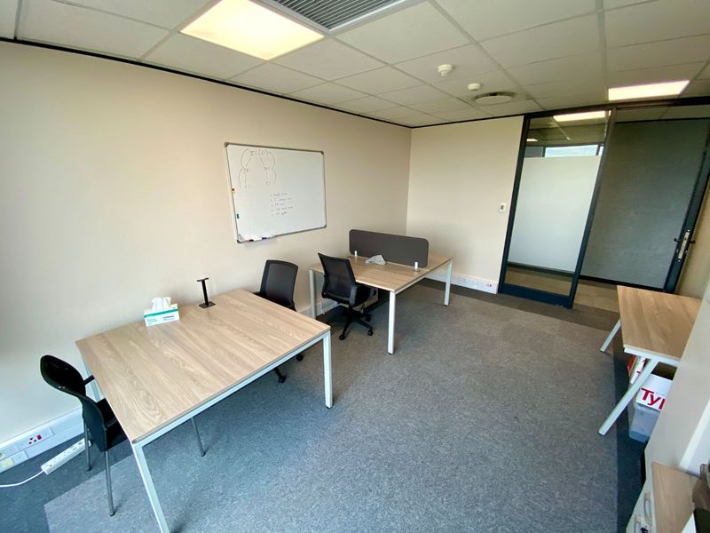 A functional commercial office space featuring carpeted flooring, a suspended ceiling with recessed lighting, and a glass partition door for natural light flow.