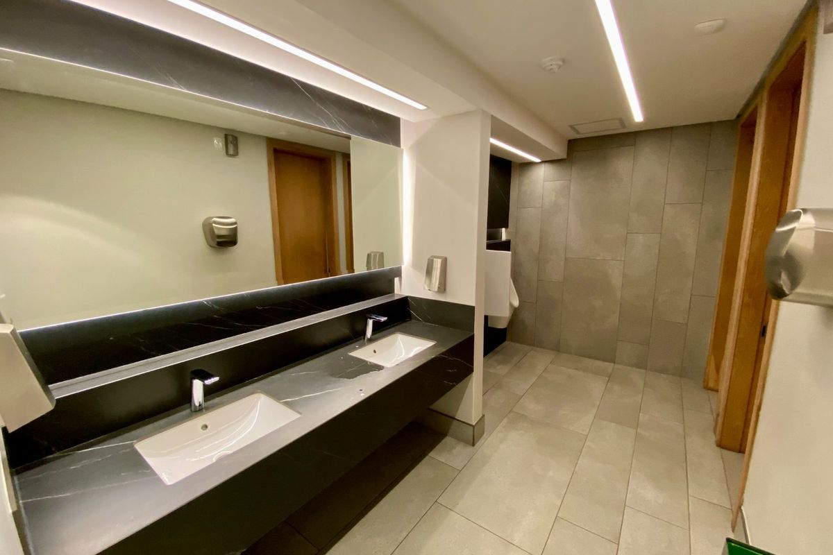 Modern commercial bathroom featuring a sleek double vanity with stone countertop, large mirror, recessed lighting, and contemporary tiled finishes.