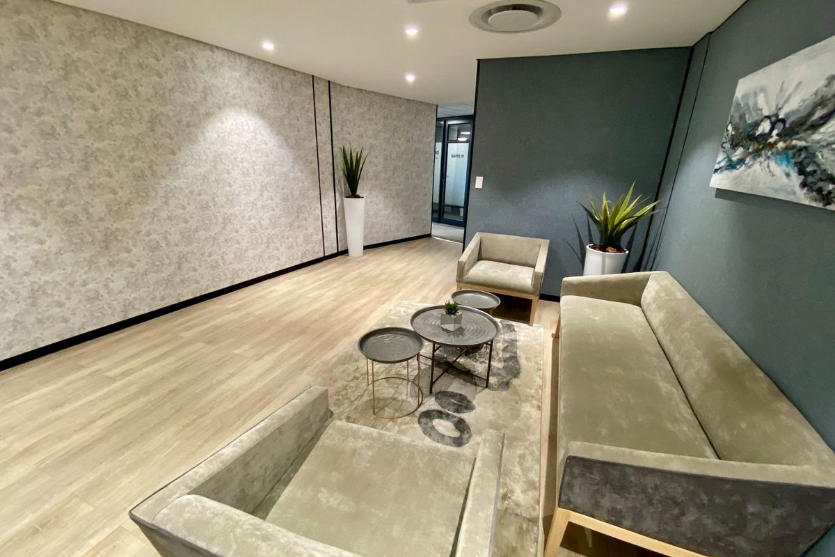 Modern commercial reception or waiting area featuring high-quality laminate flooring, recessed lighting, and contemporary wall finishes with a glass partition entrance.