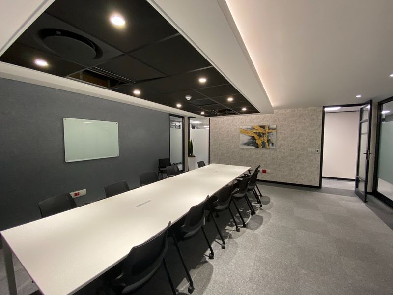 A modern commercial boardroom featuring a long conference table, recessed lighting, acoustic ceiling tiles, and glass partition doors in a professional office setting.