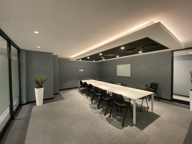 Modern commercial boardroom featuring a dropped ceiling with recessed lighting, glass partitions, and neutral grey finishes.