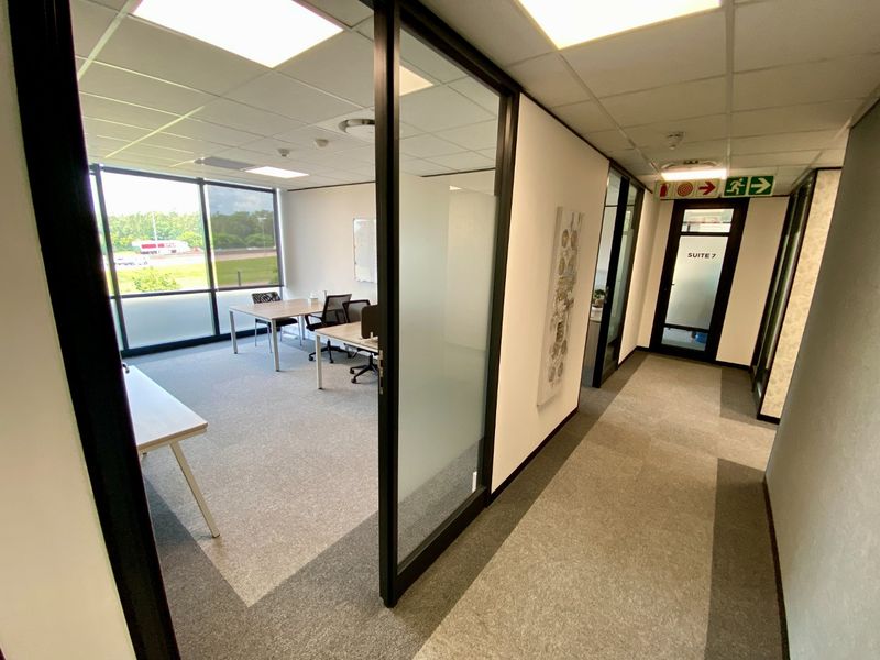 Modern commercial office suite featuring glass partitioning, suspended ceilings with recessed lighting, and large windows providing ample natural light.