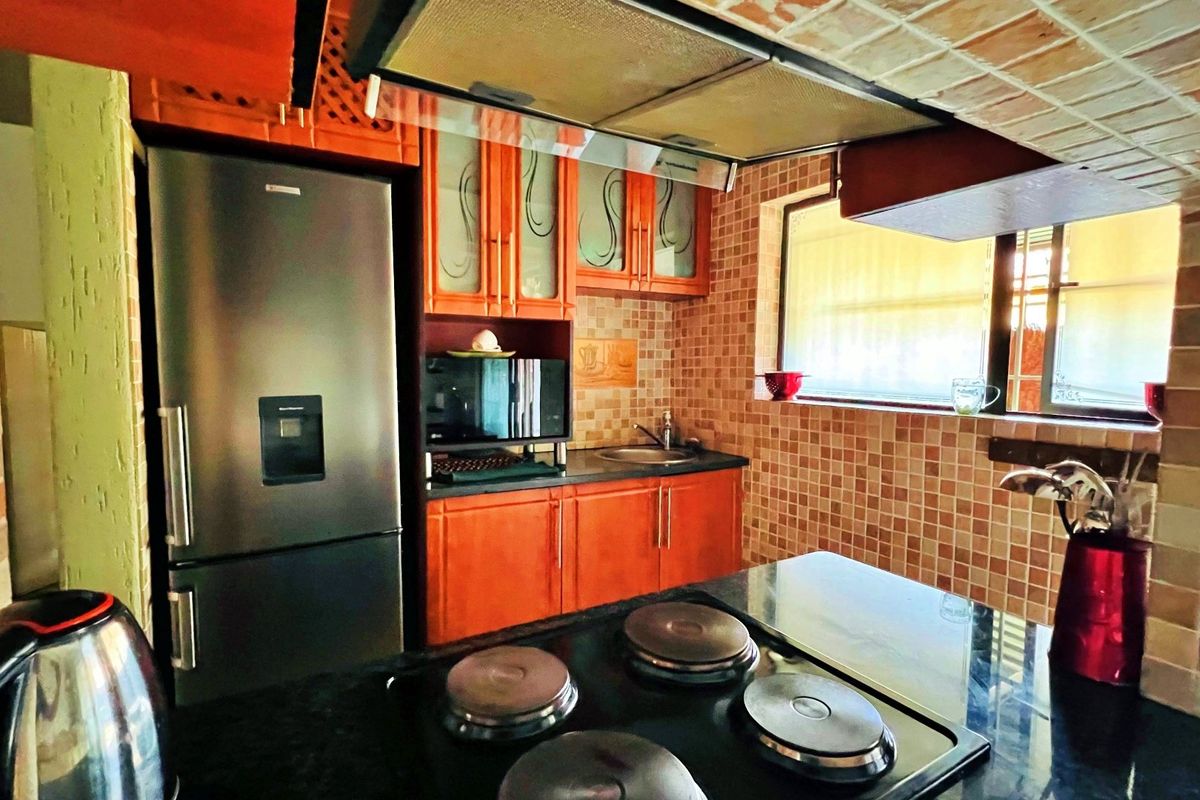 A functional kitchen featuring wooden cabinetry, granite countertops, a tiled backsplash, and a built-in electric hob with an overhead extractor fan.