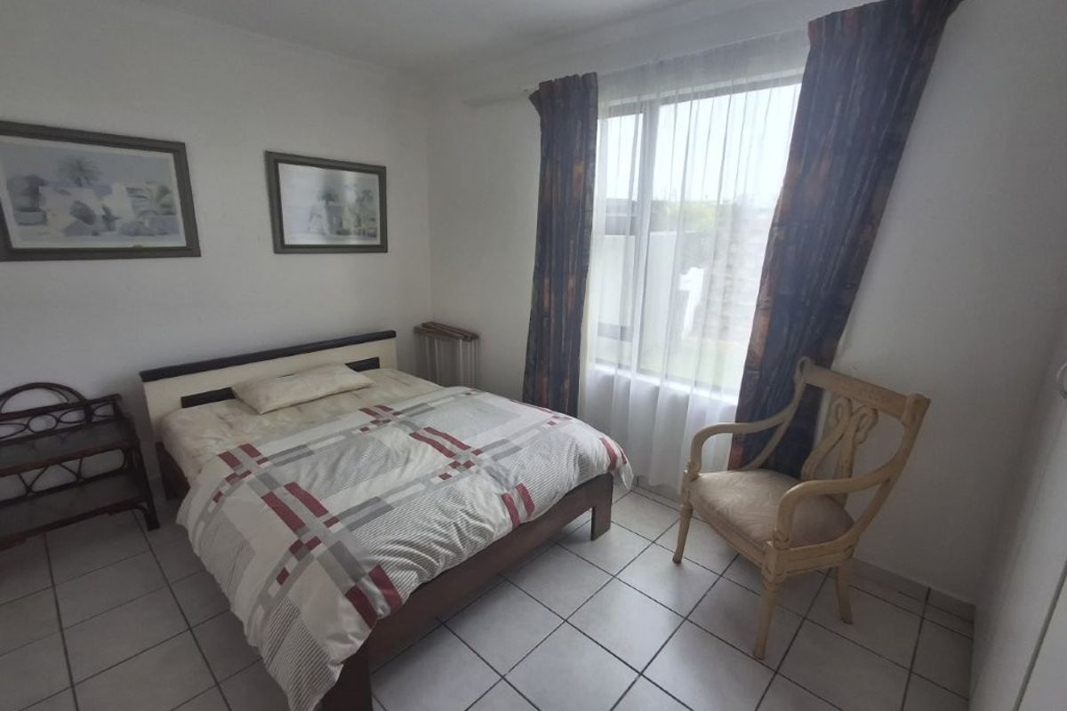 A functional bedroom featuring tiled flooring and a large window allowing natural light, providing a neutral base for potential interior updates.