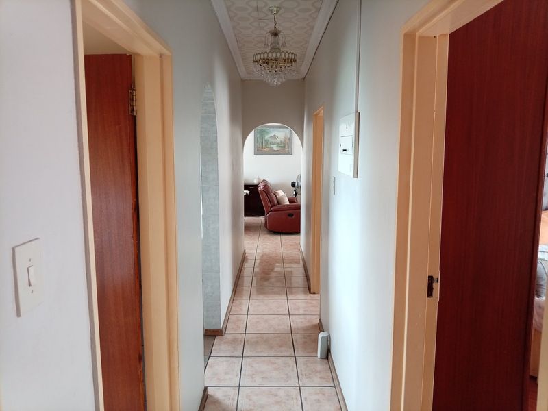 A narrow residential hallway featuring tiled flooring, arched transitions, and a central ceiling light fixture, providing access to adjacent rooms.