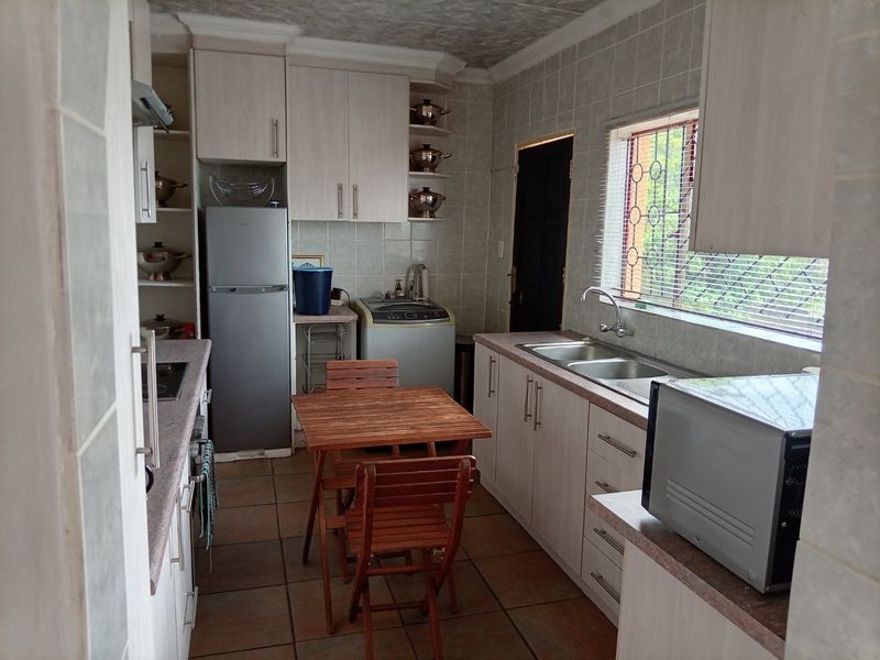 A functional kitchen featuring built-in cabinetry, tiled walls, double basin sink, and tiled flooring with direct access to an exterior door.
