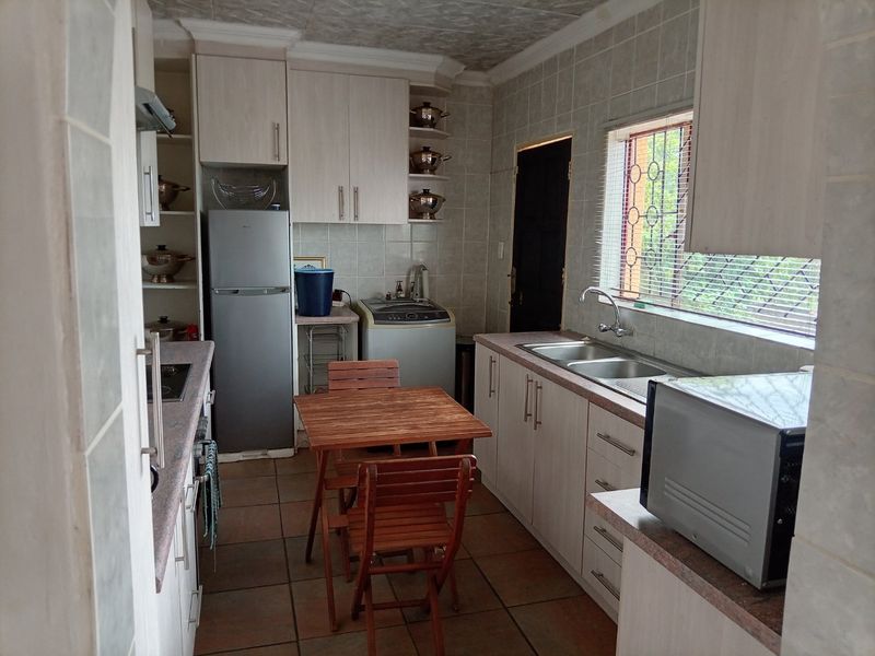 A functional kitchen featuring light-toned built-in cabinetry, a double sink, tiled backsplash, and tiled flooring with a window providing natural light.
