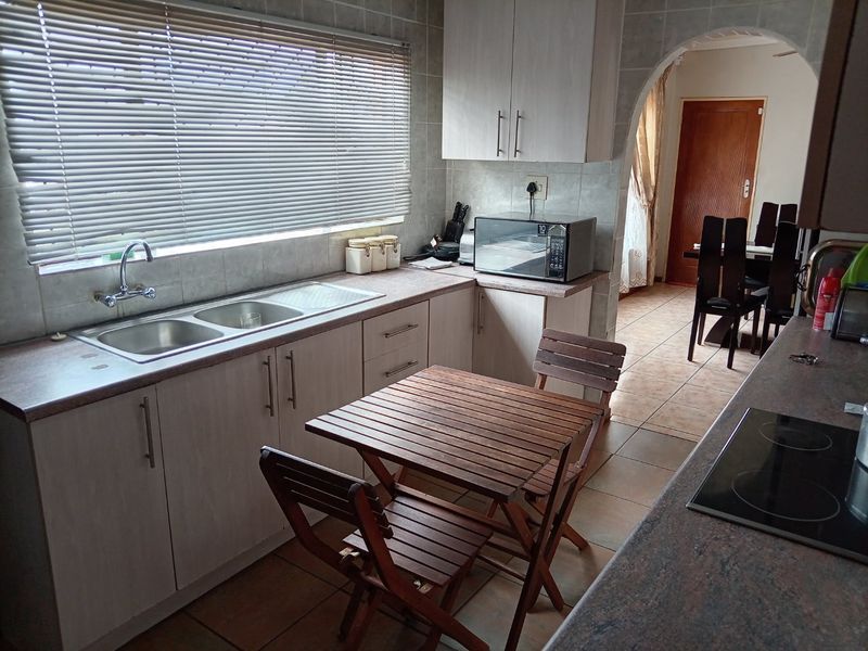 A functional kitchen featuring laminate countertops, double bowl sink, built-in cabinetry, and ceramic tiling, with an arched doorway leading to the dining area.
