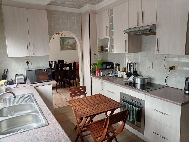 Functional kitchen featuring light-toned cabinetry, laminate countertops, integrated oven and hob, and a tiled backsplash, with an arched opening leading to the dining area.