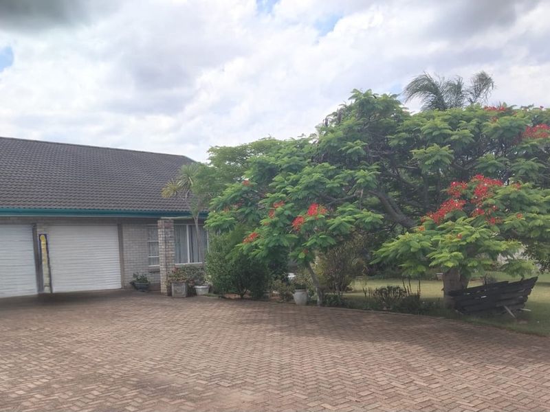 Front view of a residential property featuring a double garage, brick paved driveway, and established garden with mature trees.