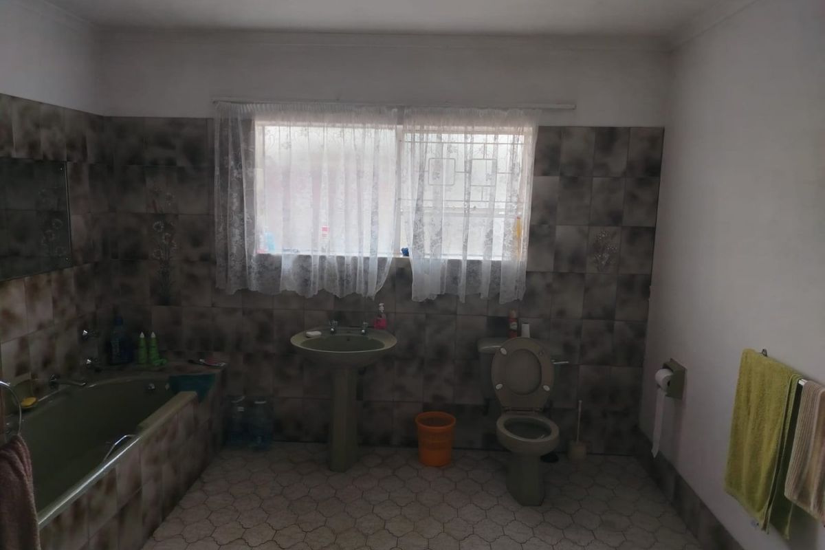 A dated bathroom featuring a bathtub, pedestal basin, and toilet with patterned wall tiles and tiled flooring.