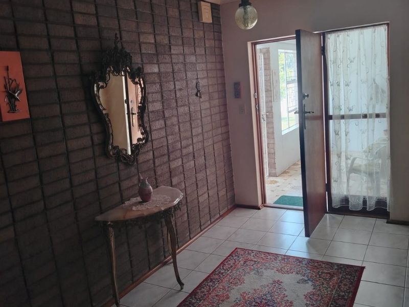 Entrance foyer featuring a textured exposed brick wall, neutral tiled flooring, and a direct view through the front door to the exterior.