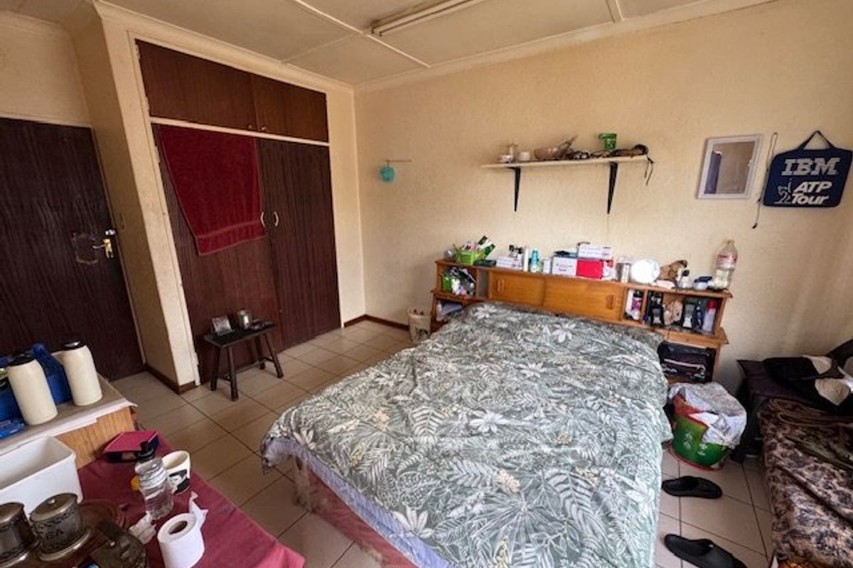 A bedroom featuring built-in cupboards and tiled flooring, offering a functional space with potential for cosmetic updates.